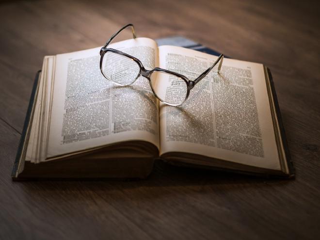 An open book flat on a table, with reading glasses perched on the pages